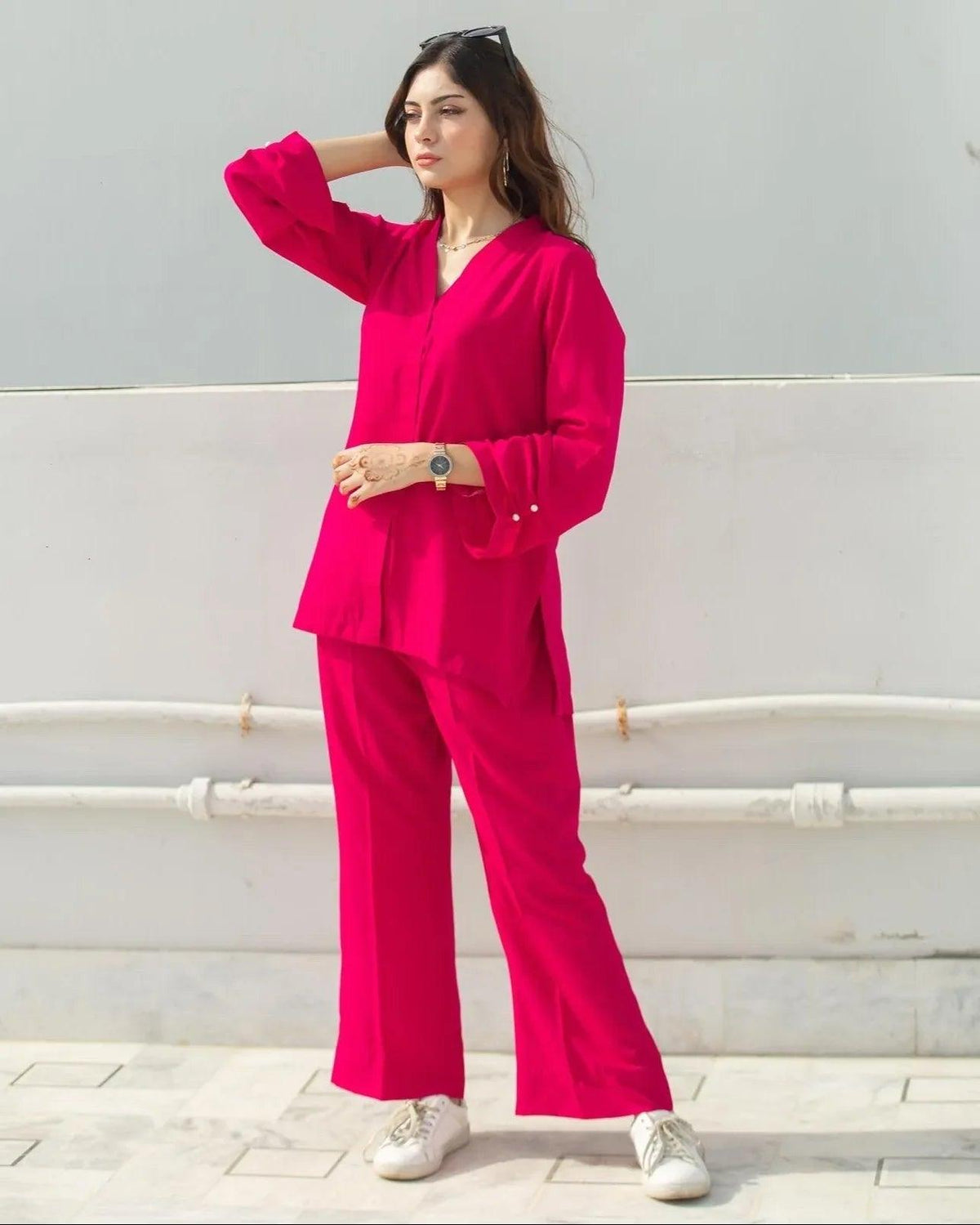 Woman wearing a bright pink outfit with white shoes against a light gray wall.