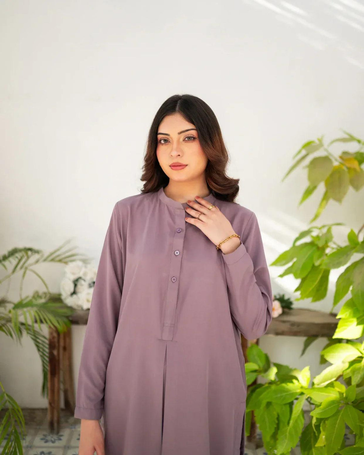 Woman wearing a mauve dress standing in a room with plants