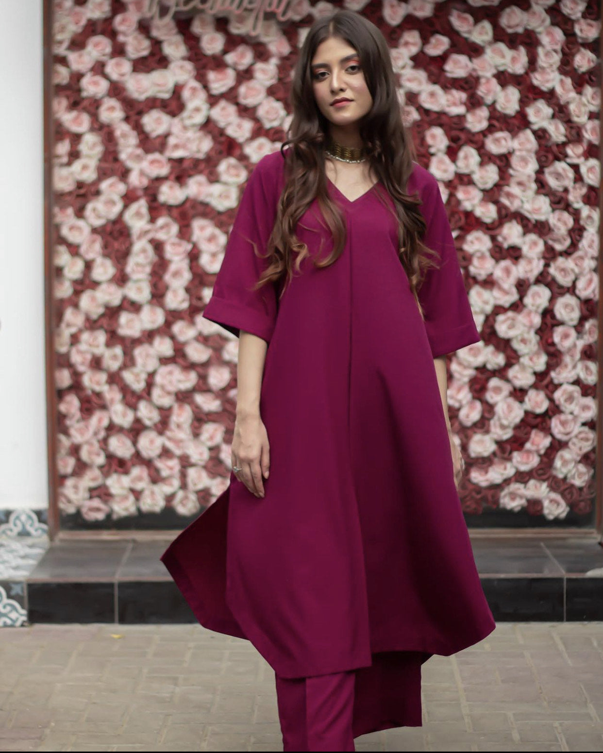 A woman in a magenta stitched dress standing confidently, showcasing her stylish outfit.