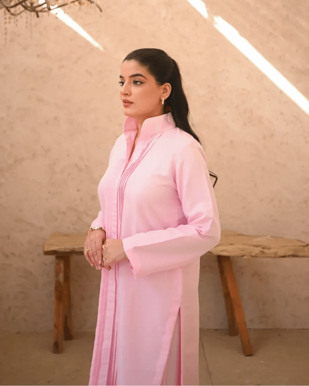 A woman standing in a sunny area wearing a pink two-piece rawsilk dress with long sleeves and pink stripes.