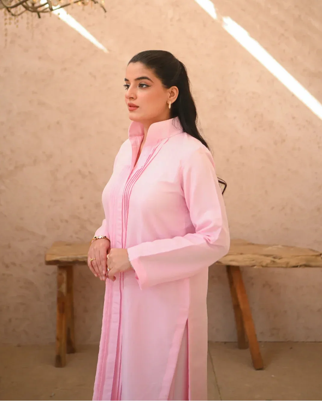 A woman standing in a sunny area wearing a pink two-piece rawsilk dress with long sleeves and pink stripes.