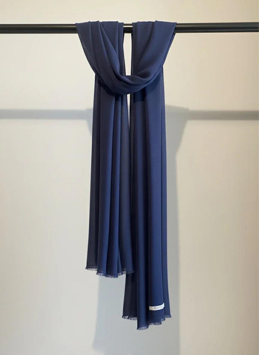 Navy blue scarf draped over a black rod against a light gray background