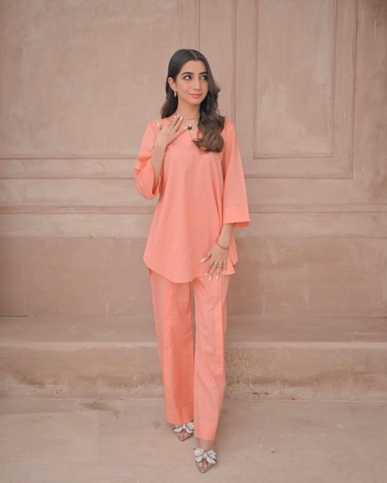 Woman wearing a peach outfit against a beige wall