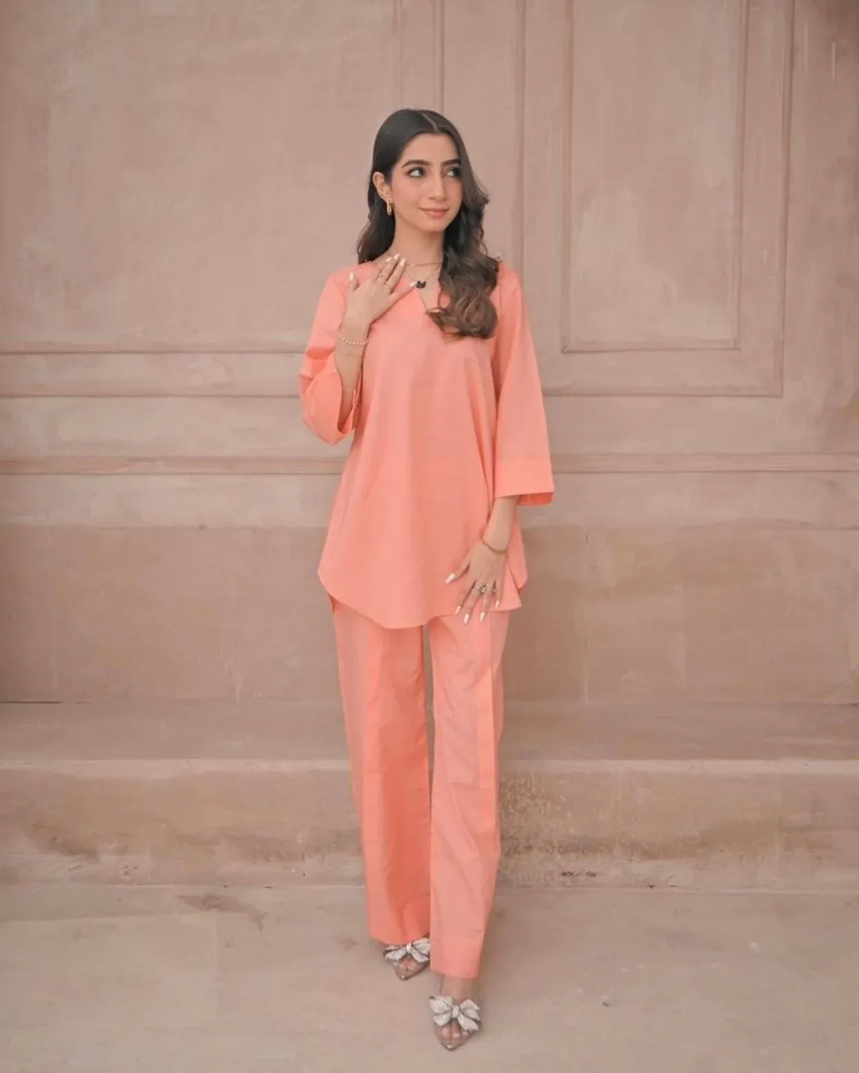 Woman wearing a peach outfit against a beige wall