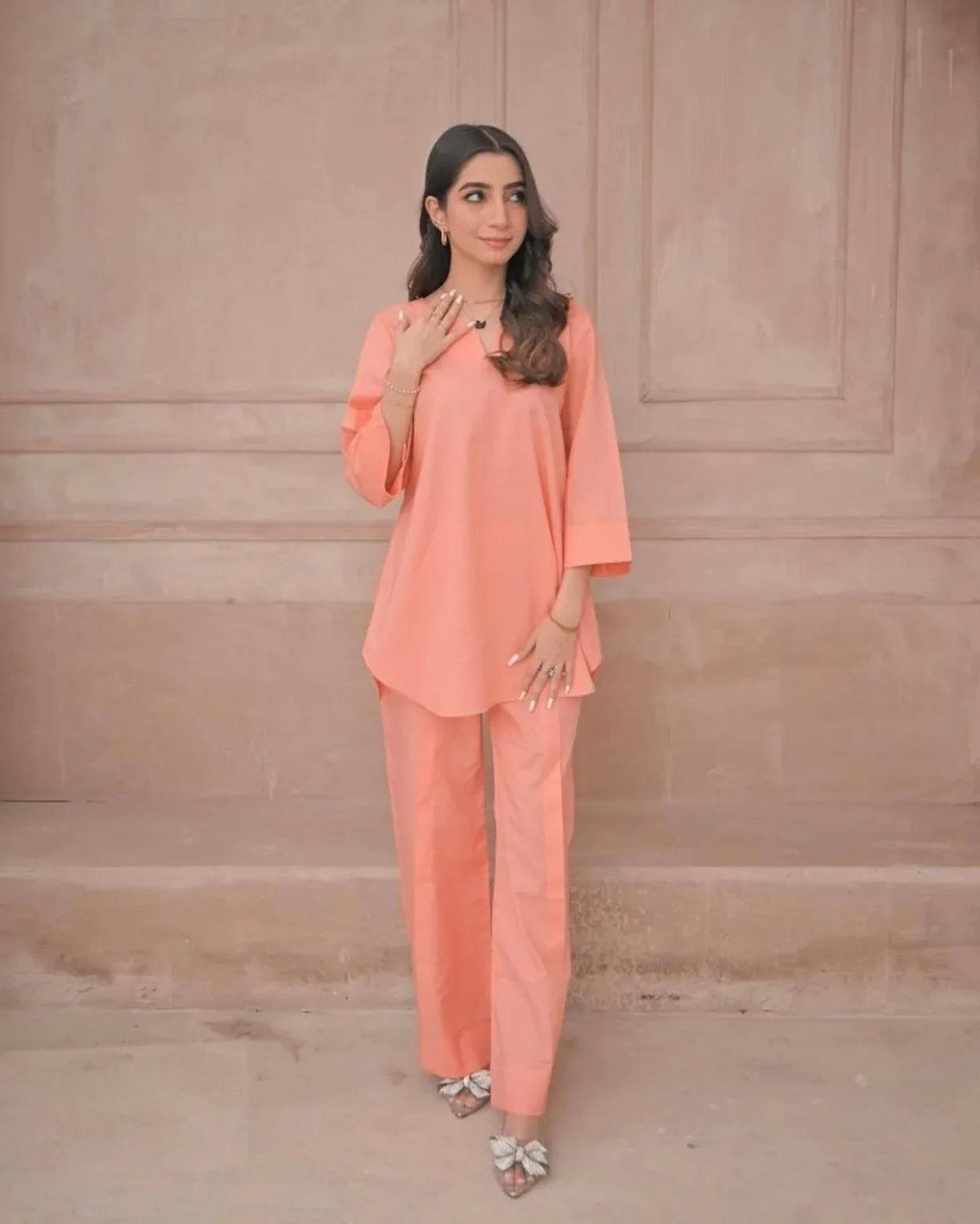 Woman wearing a peach outfit against a beige wall