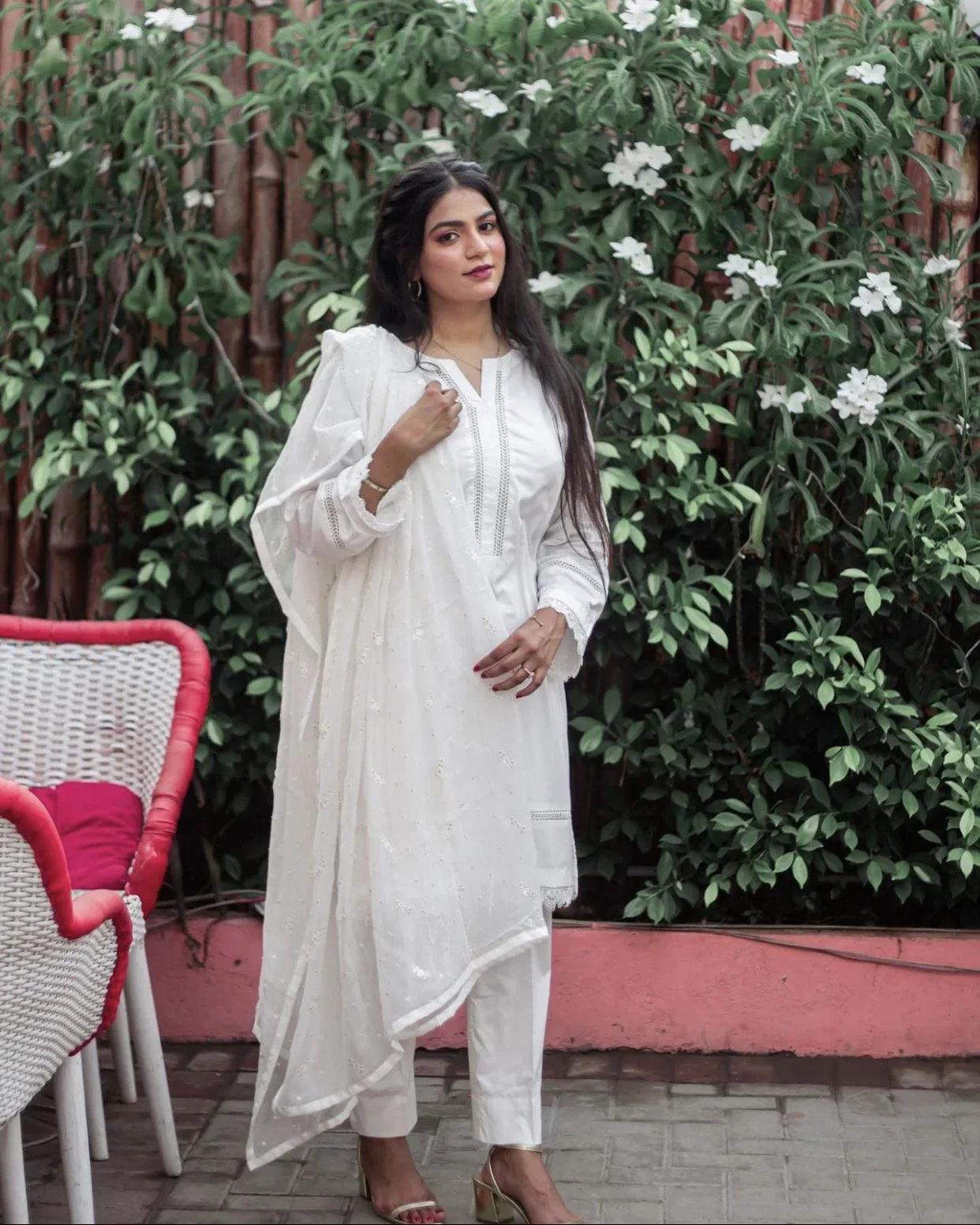 A woman in white three piece dress walking outdoor on a sunny day, surrounded by greenery.