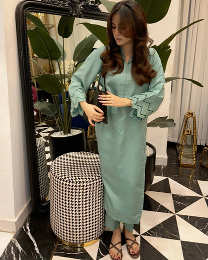 Woman in a Apple Green dress standing in a stylish room with plants and decor.