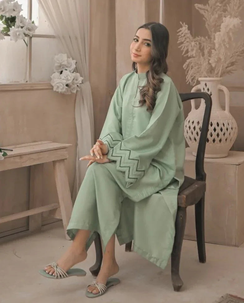 A Woman wearing an apple green dress with embroidery on sleeves and zigzag cuffs, smiling confidently. sitting on a chair.