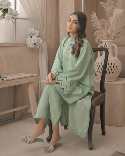 A Woman wearing an apple green dress with embroidery on sleeves and zigzag cuffs, smiling confidently. sitting on a chair.