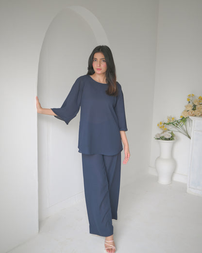 A woman in a navy blue outfit stands next to an arched alcove in a minimalist white room.