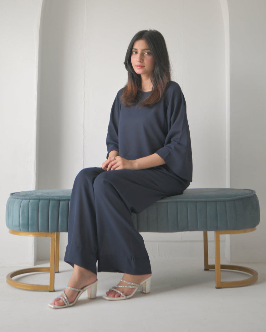 A woman in a navy blue outfit sitting next to an arched alcove in a minimalist white room.