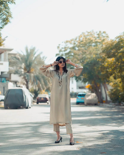 Woman in a beige dress standing on a street with trees and buildings in the background