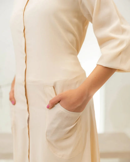 Fawn dress with a close-up of a hand in a pocket against a blurred background