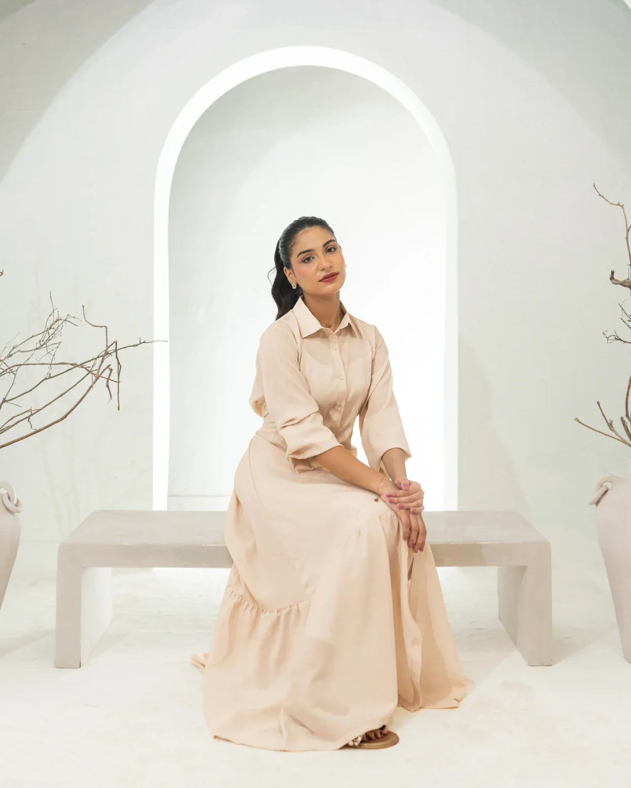Woman in a fawn dress sitting on a white bench with a white archway in the background