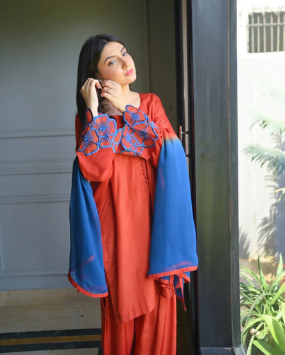 Women wearing a three piece orange dress with embroidery on sleeves.