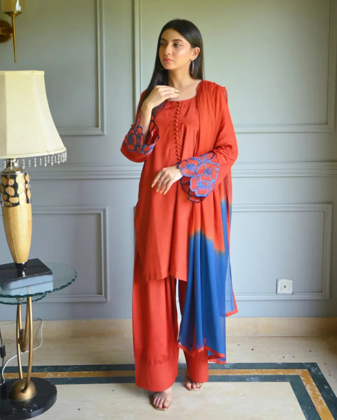 Women wearing a three piece orange dress which includes Farshi Shalwar kameez with embroidery on sleeves, and a two tone dyed chiffon dupatta.
