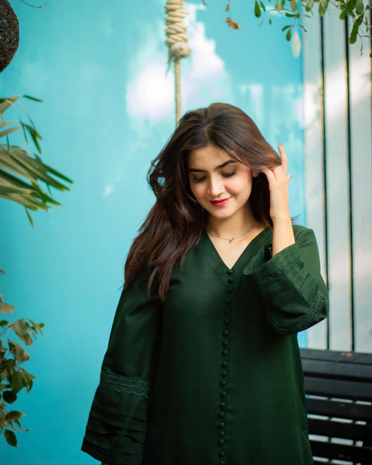 Woman in a bottle green dress against a blue background with plants