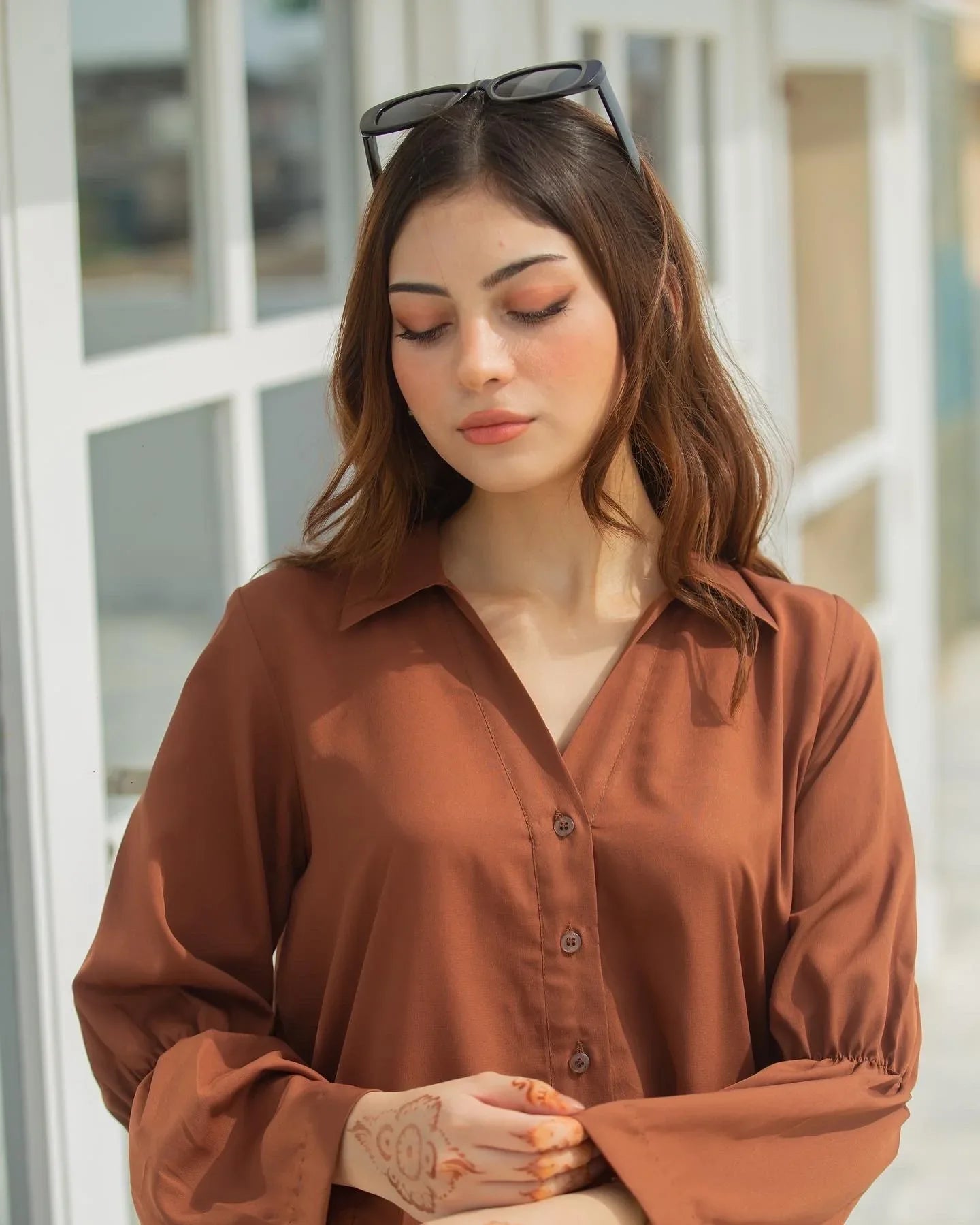 Woman in a brown dress standing in front of a white building with large windows.