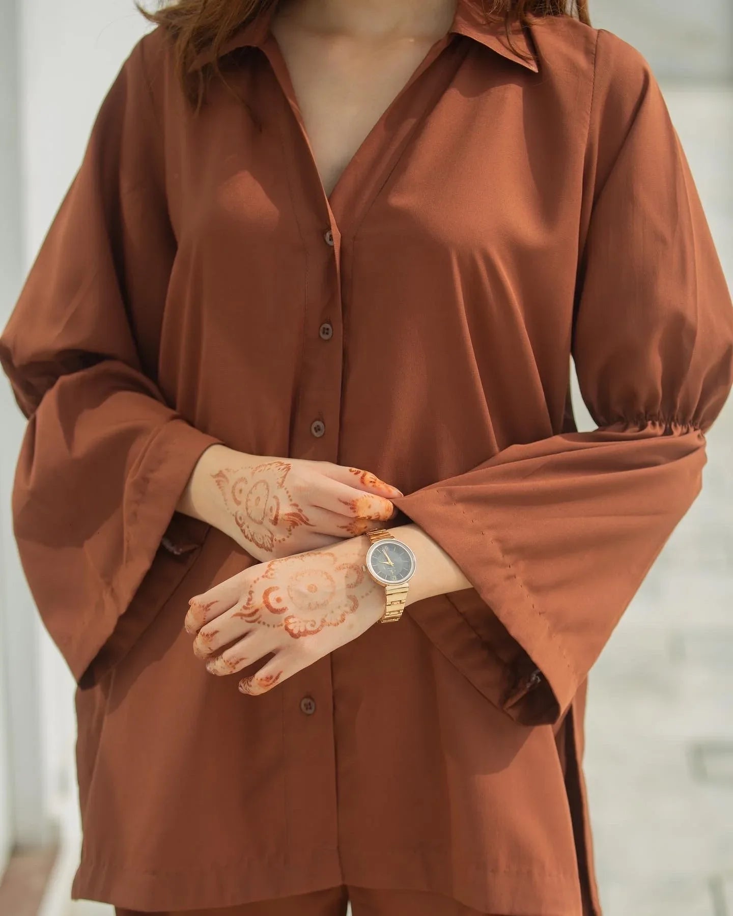 Woman in a brown button down shirt standing in front of a white wall.