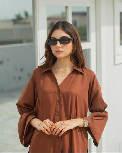 Woman in a brown button down shirt standing in front of a white building with large windows.