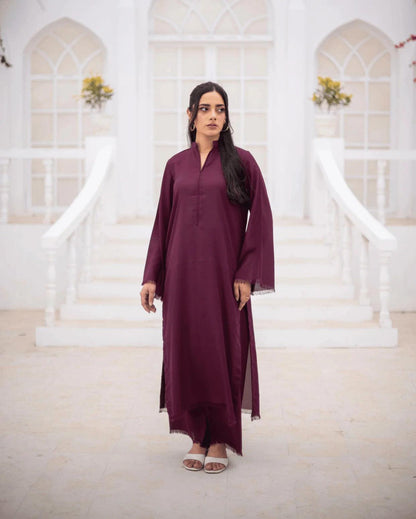 A woman wearing a long-sleeved, burgundy co ord set stands in front of a white arched building with steps.