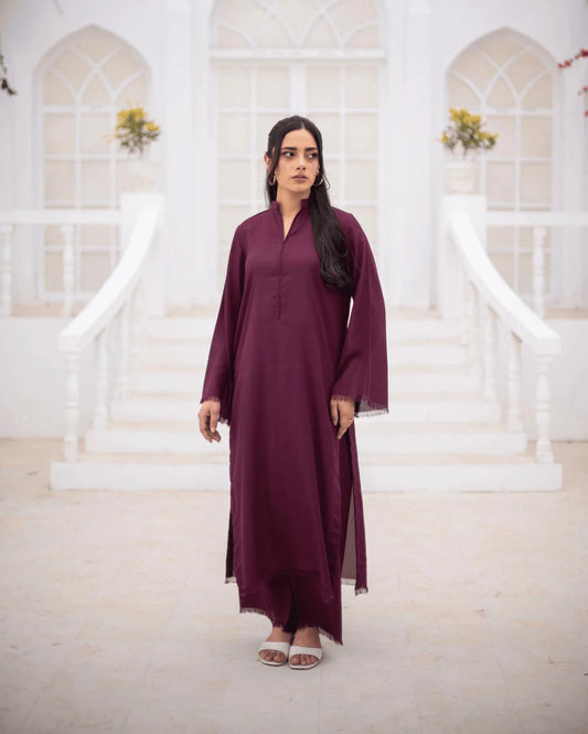 A woman wearing a long-sleeved, burgundy co ord set stands in front of a white arched building with steps.