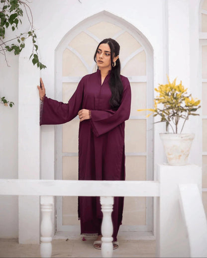 A woman wearing a long-sleeved, burgundy co ord set, standing in a white arched doorway with decorative plants on either side.