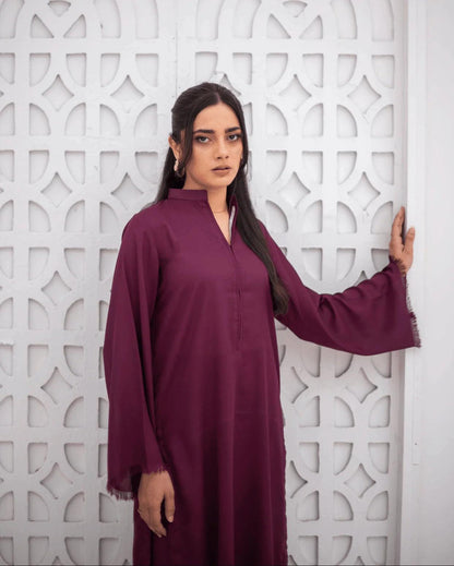 A woman wearing a long-sleeved, burgundy co ord set stands in front of a white geometric patterned screen.