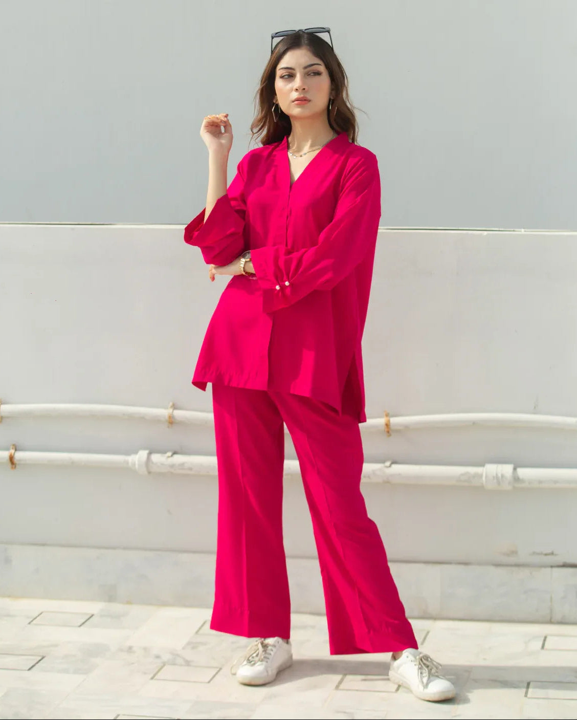 Woman wearing a bright pink outfit with white shoes against a light gray wall.