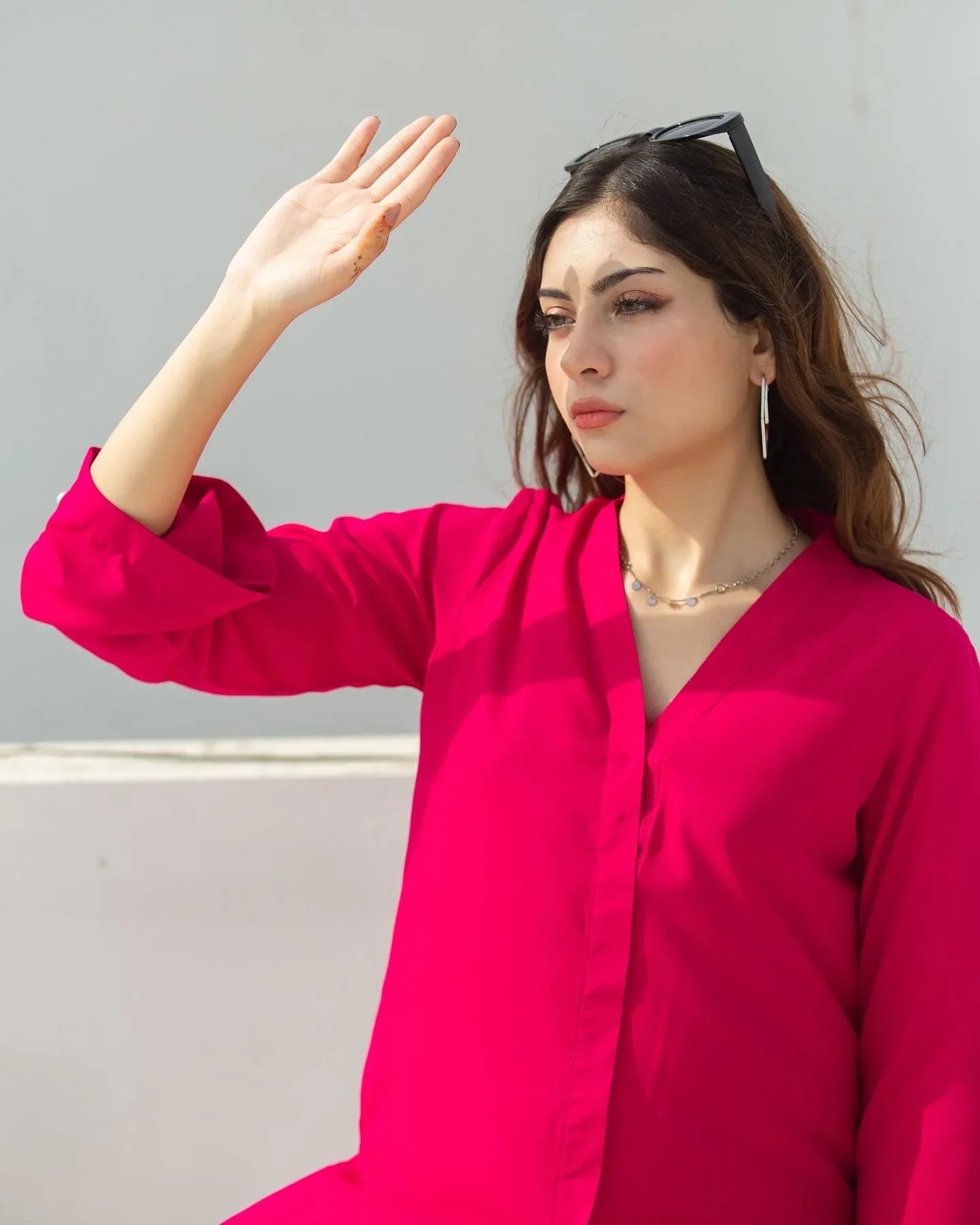 Woman wearing a bright pink outfit against a light gray wall.