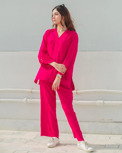 Woman wearing a bright pink outfit with white shoes against a light gray wall.