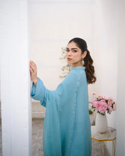 A woman wearing a Sky Blue rawsilk fabric shirt with chiffon dupatta. The dress is embellished with stone details.
