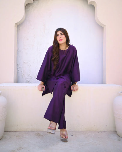 Woman in a purple outfit sitting on a white ledge with a light-colored wall behind her.