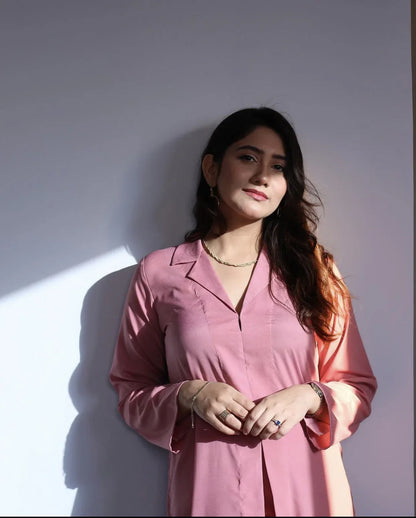 Woman in a pink outfit standing in a well-lit room with a neutral background.