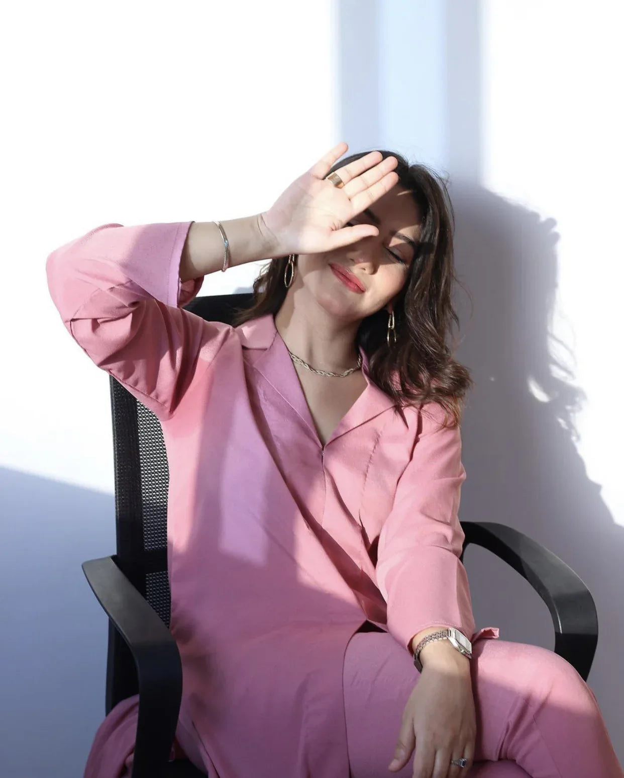 Woman in a pink outfit sitting in a well-lit room with a neutral background