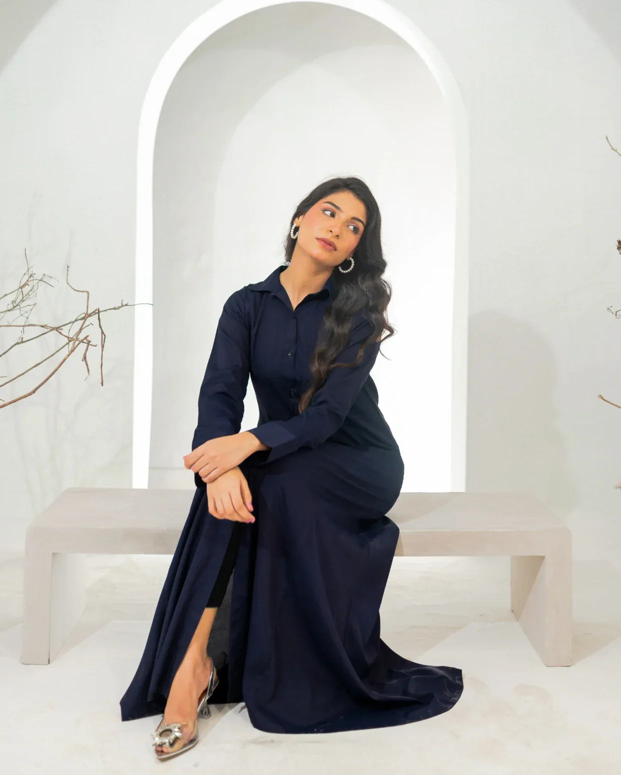 Woman in a navy blue dress sitting on a white bench with a white archway in the background