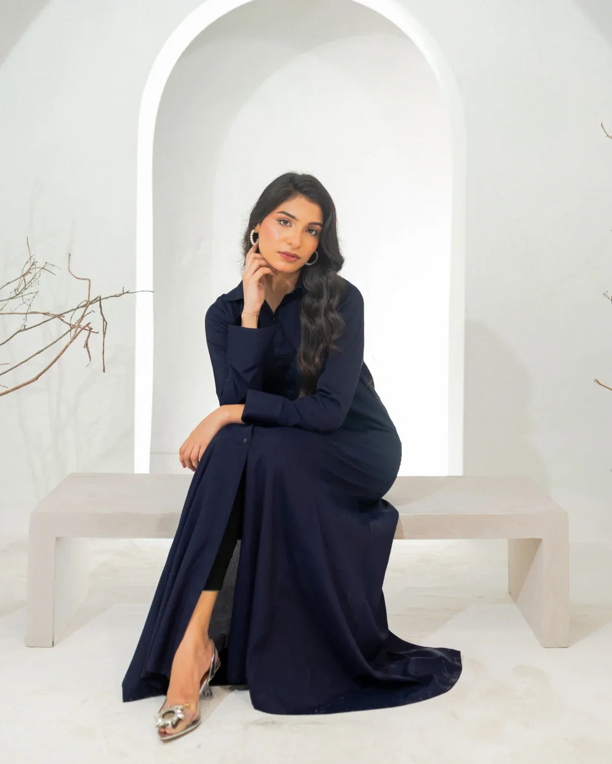 Woman in a navy blue dress sitting on a white bench in a minimalistic setting.