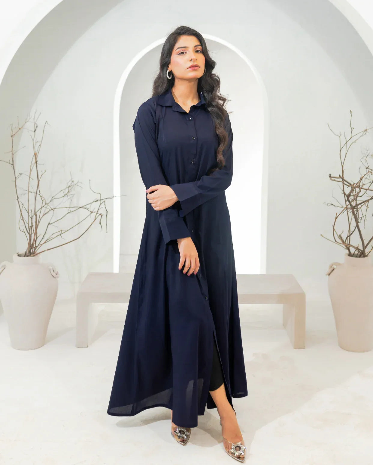 Woman wearing a navy blue dress in a white room with arches and plants.