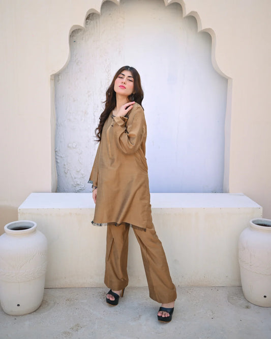 Woman in a beige outfit standing in front of an arched stone wall.