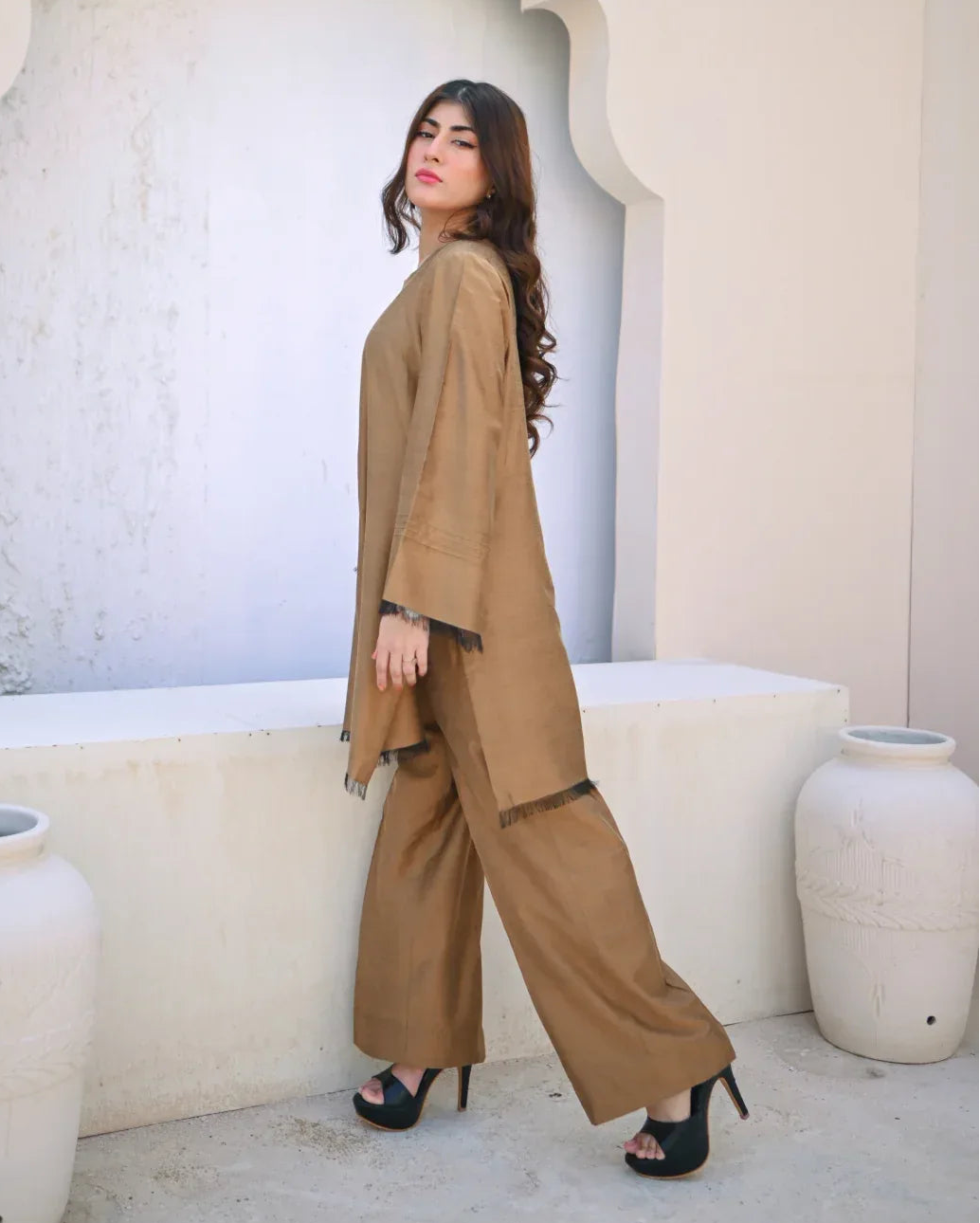 Woman in a beige outfit standing in front of a decorative wall with white vases.