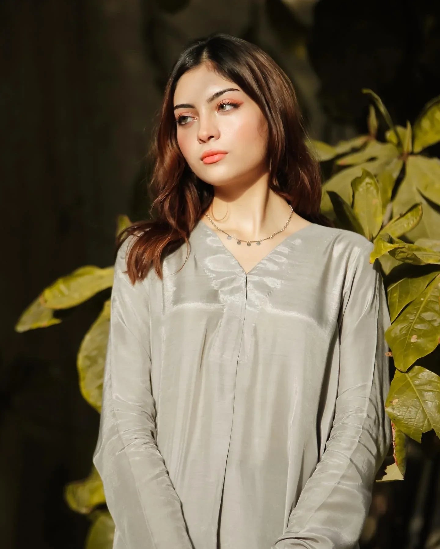 Women wearing a grey dress with leaves in the background.