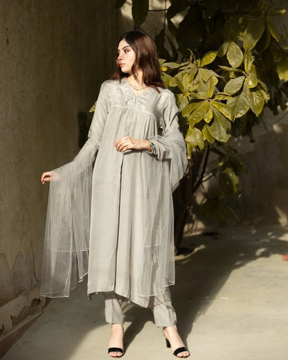 Women wearing a grey three piece dress with a tree in the background.