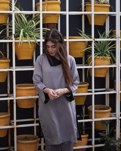 Woman in a gray dress stands in front of a grid of vibrant yellow pots with green plants. 