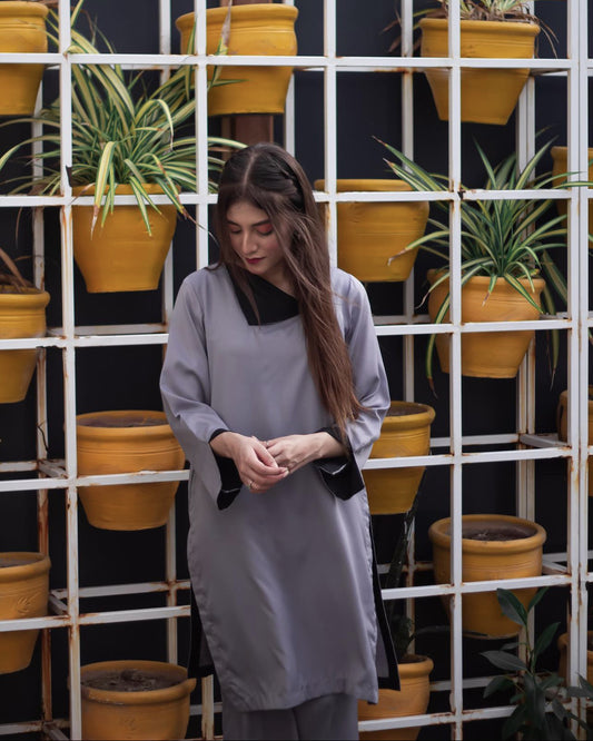 Woman in a gray dress stands in front of a grid of vibrant yellow pots with green plants. 
