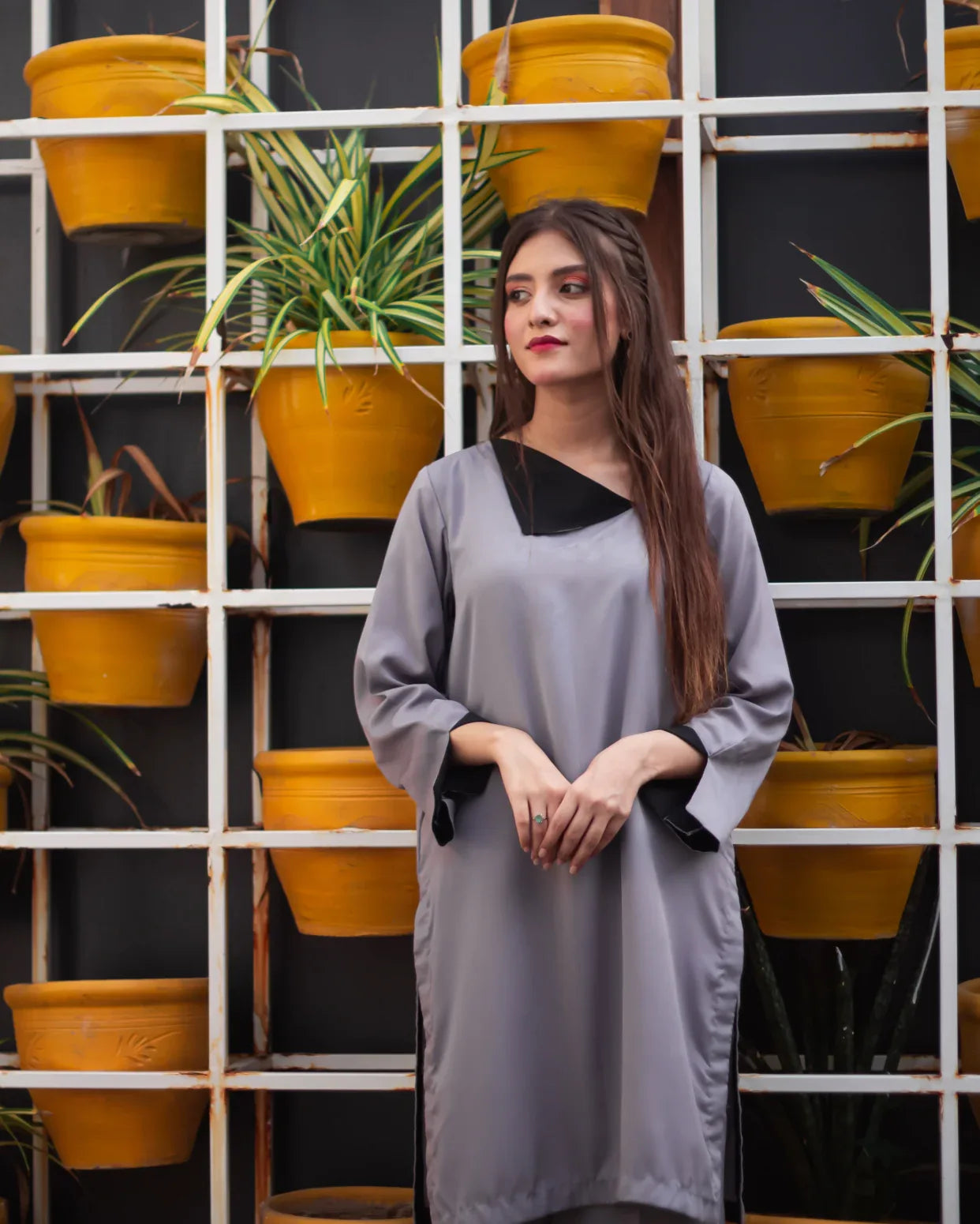 Woman in a gray dress standing in front of a wall with yellow pots and plants