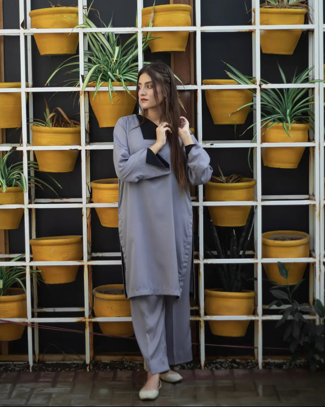 Woman in a gray dress stands in front of a grid of vibrant yellow pots with green plants. 