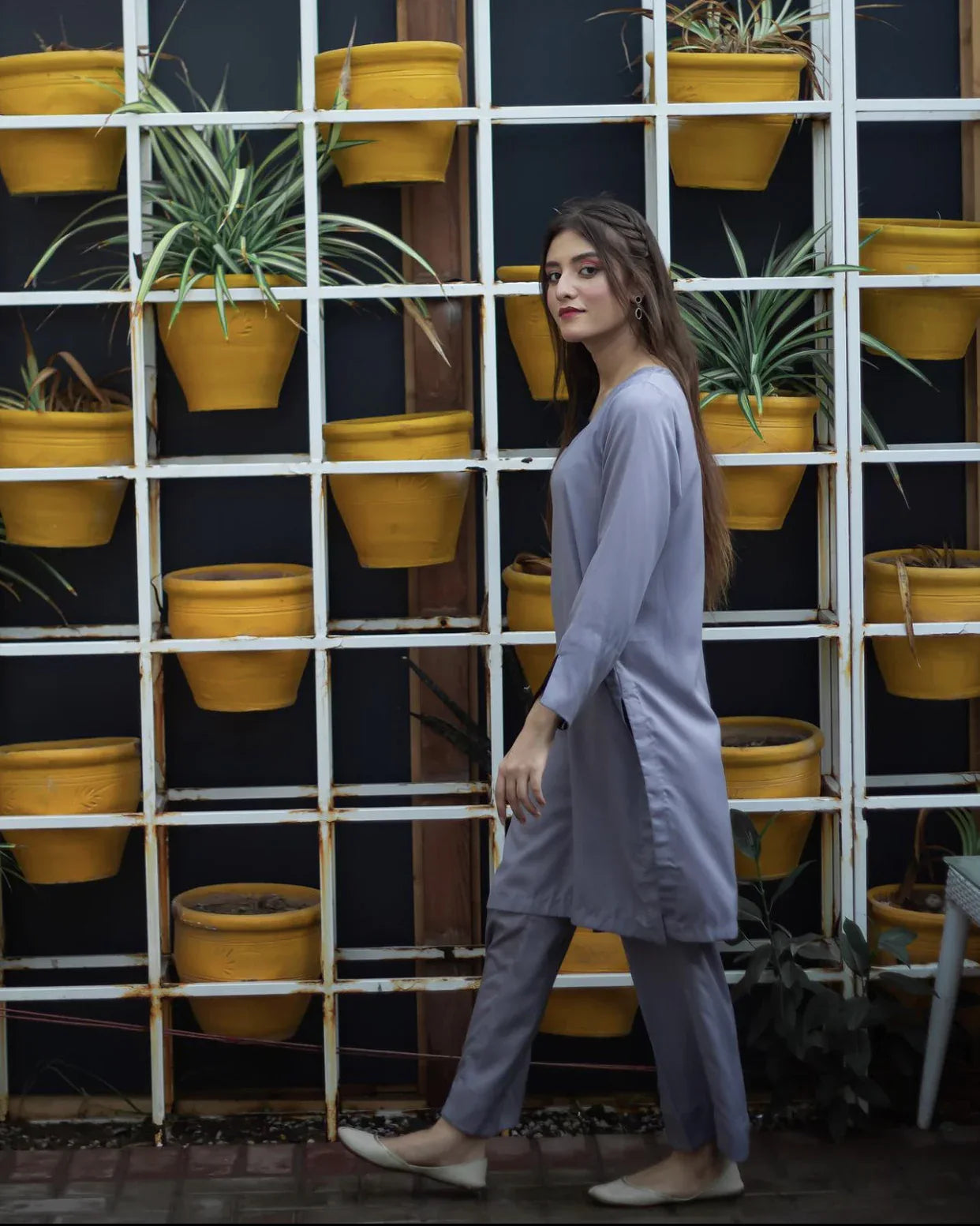 Woman in a gray dress walking in front of a grid of vibrant yellow pots with green plants. 
