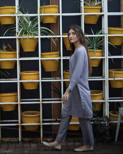 Woman in a gray dress walking in front of a grid of vibrant yellow pots with green plants. 