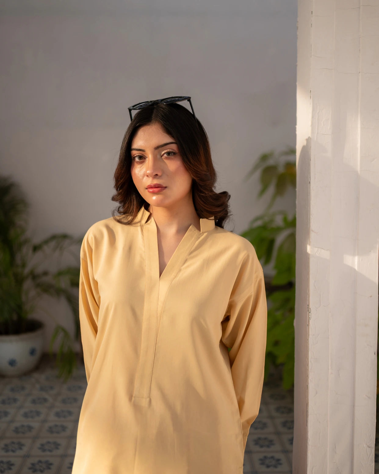 Woman wearing a lemon yellow top with sunglasses on her head, standing indoors.