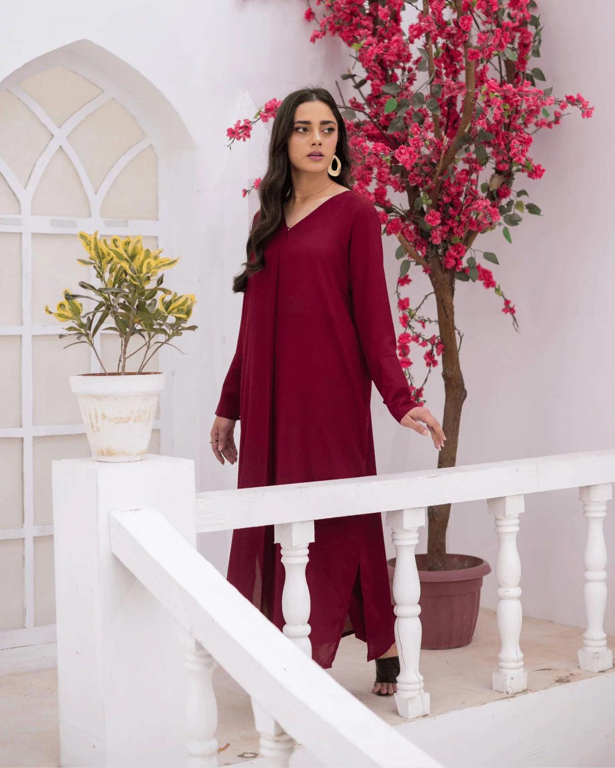 A woman modeling a long-sleeved, magenta co ord set in a bright, modern white architectural setting with a potted pink tree and white railing.